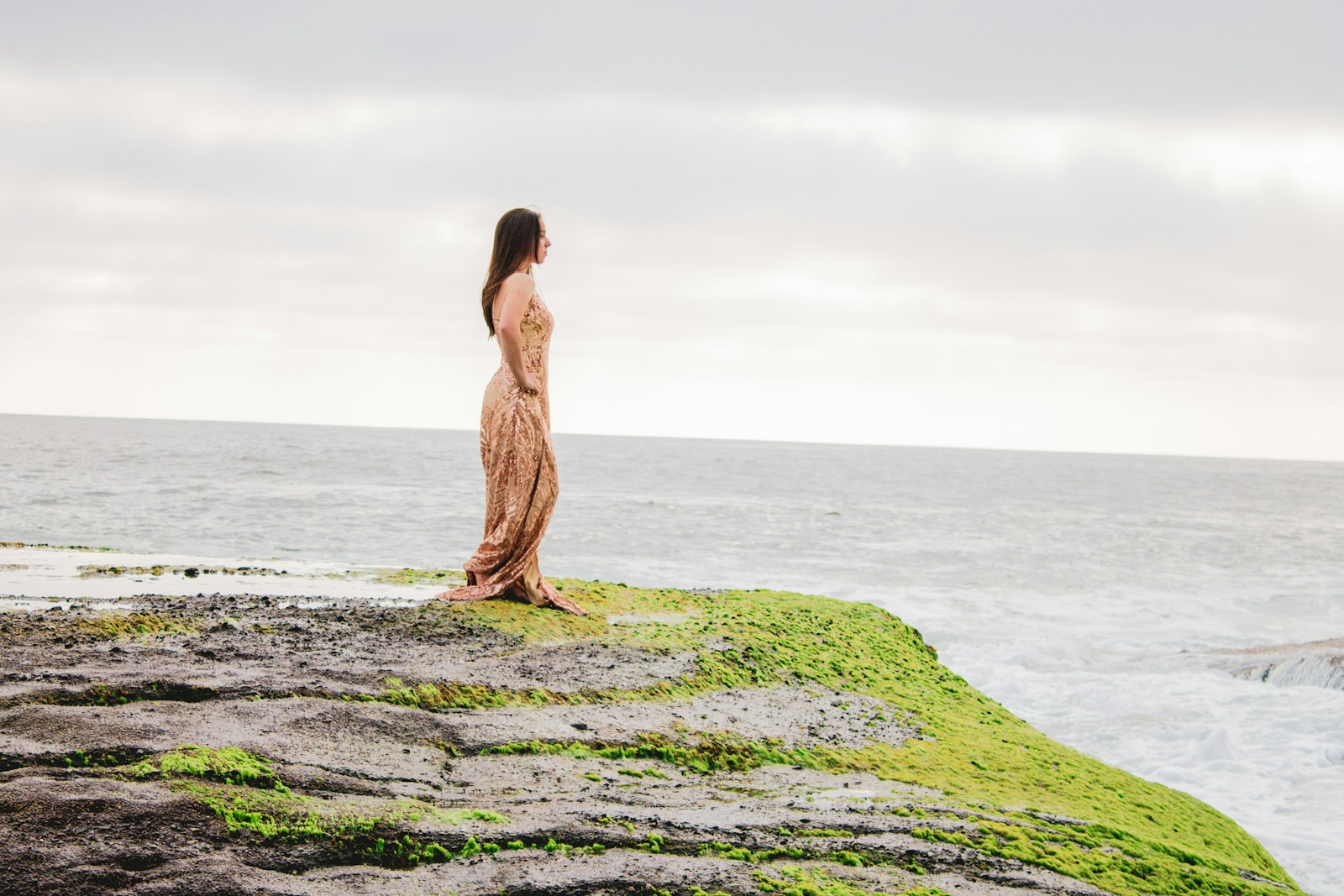 Photo by Emmanuel Olguín woman in brown dress standing on green moss near body of water during daytime
